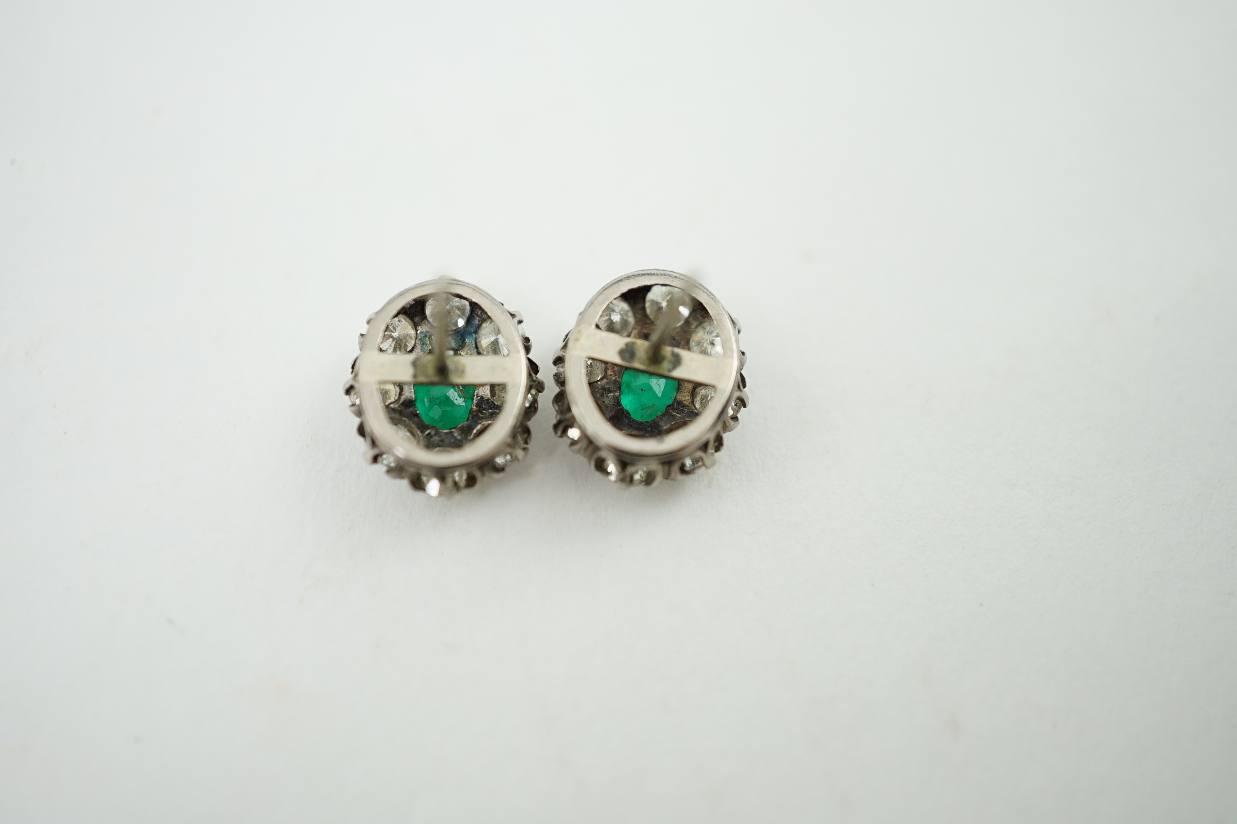 A pair of white gold, single stone emerald and eight stone diamond set oval cluster earrings